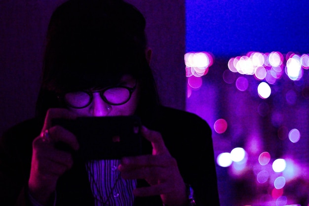 Foto primer plano de una mujer joven usando un teléfono inteligente en el cuarto oscuro por la noche