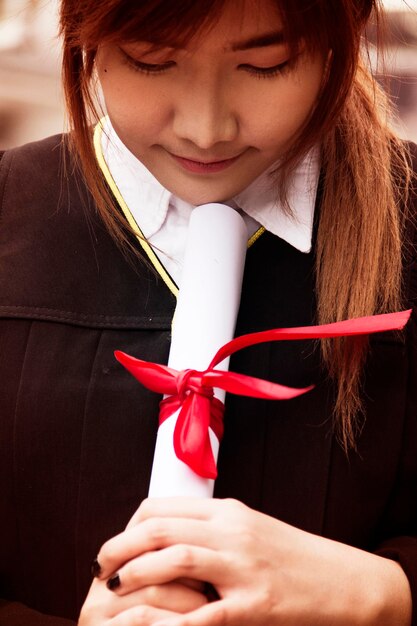 Primer plano de una mujer joven en vestido de graduación con un título