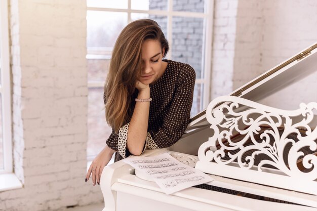 Primer plano de una mujer joven en un vestido marrón apoyado en un piano
