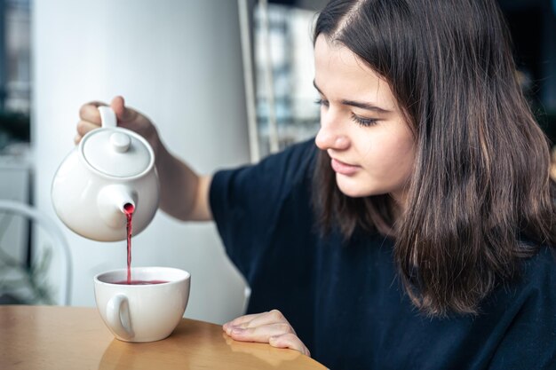 El primer plano de una mujer joven vierte té de una tetera