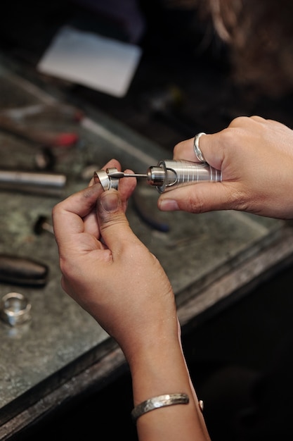 Primer plano de una mujer joyero con las manos sucias limpieza anillo de plata con pulidora en taller oscuro