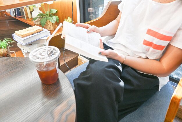 Primer plano de una mujer leyendo un libro con café frío en la cafetería Mindfulness living Autocuidado intelectual