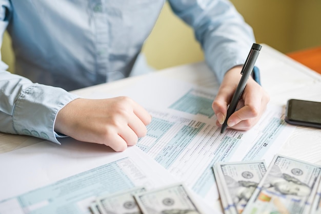 Primer plano de una mujer llenando un formulario 1040 mientras está sentado en una mesa Documento financiero del concepto de impuestos
