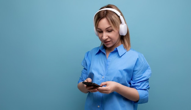 Primer plano de una mujer milenaria en una camisa casual con grandes auriculares blancos con un teléfono inteligente en ella