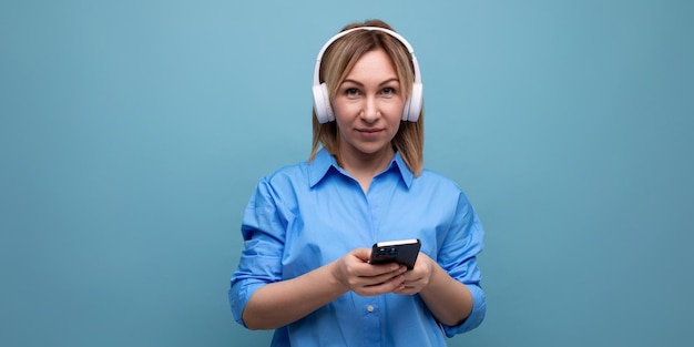 Primer plano de una mujer milenaria en una camisa casual con grandes auriculares blancos con un teléfono inteligente en ella