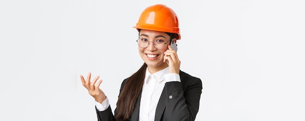 El primer plano de una mujer de negocios asiática administra un ingeniero empresarial con casco de seguridad y se adapta a una conversación telefónica llamando a los inversores sonriendo mientras habla sobre el fondo blanco del teléfono inteligente