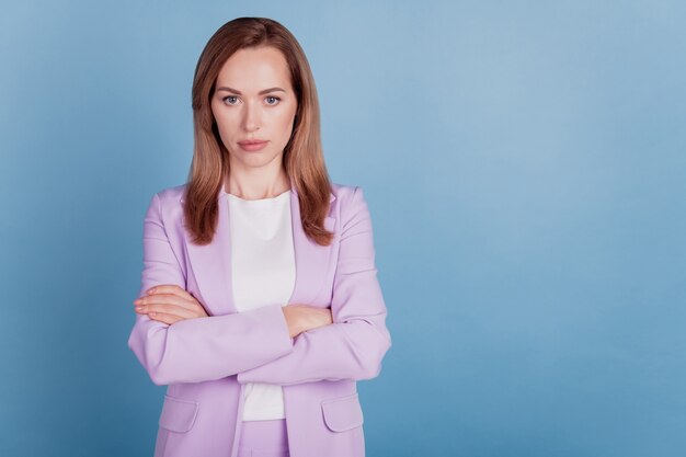 Primer plano de una mujer de negocios confiada mira la cámara con las manos cruzadas sobre fondo azul.