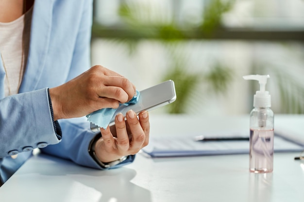 Primer plano de una mujer de negocios desinfectando su teléfono inteligente en la oficina