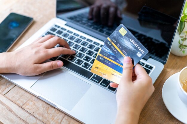 Primer plano de una mujer de negocios de personas independientes Mano que sostiene tarjetas de crédito trabajo informal usando una computadora portátil con una taza de café en una cafetería como el concepto de compra de pago en línea de fondo