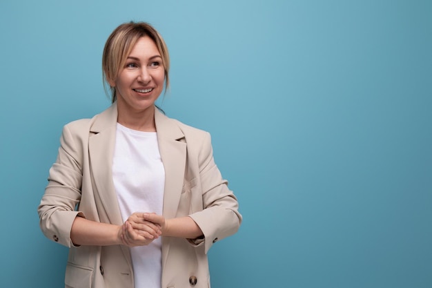 Primer plano de una mujer de negocios rubia sonriente positiva en una chaqueta exitosa en el trabajo en el fondo