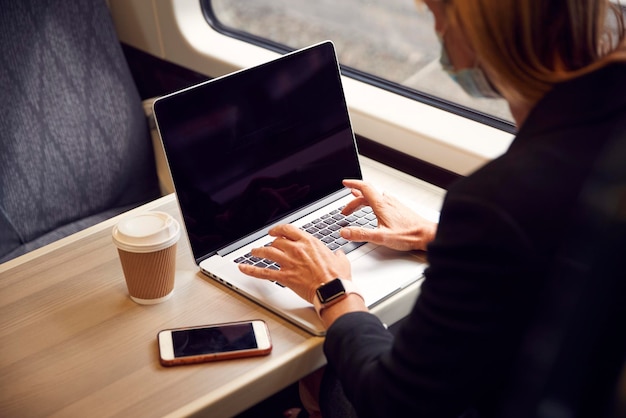 Primer plano de una mujer de negocios en un tren que trabaja en una computadora portátil usando una máscara facial de PPE durante la pandemia de salud