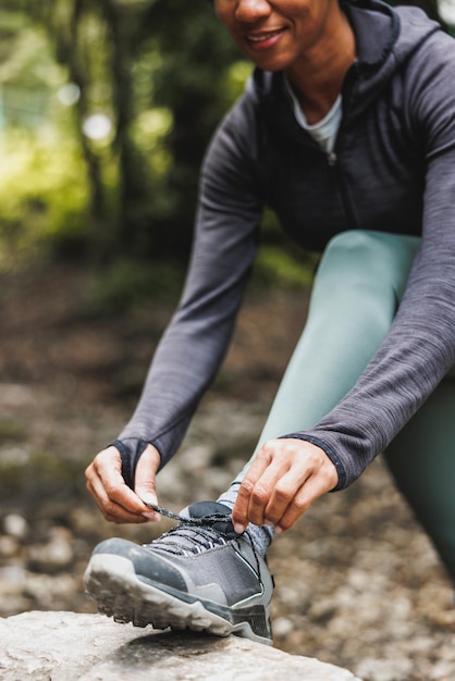 Primer plano de una mujer negra irreconocible atando sus zapatillas en el bosque durante una caminata o trotando en la montaña.