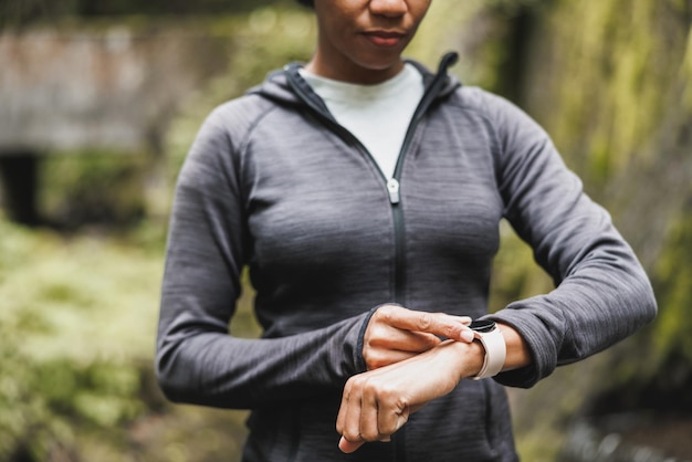 Primer plano de una mujer negra irreconocible mirando el reloj inteligente y preparándose para hacer jogging en la naturaleza.