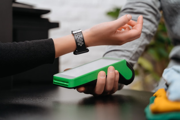 Primer plano de una mujer pagando la compra a través de un reloj inteligente con tecnología NFC en una tienda de ropa