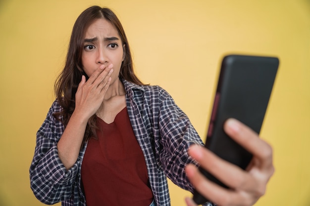 Primer plano de una mujer con el pelo largo que usa un teléfono móvil se sorprende cuando ve la pantalla de un teléfono móvil ...