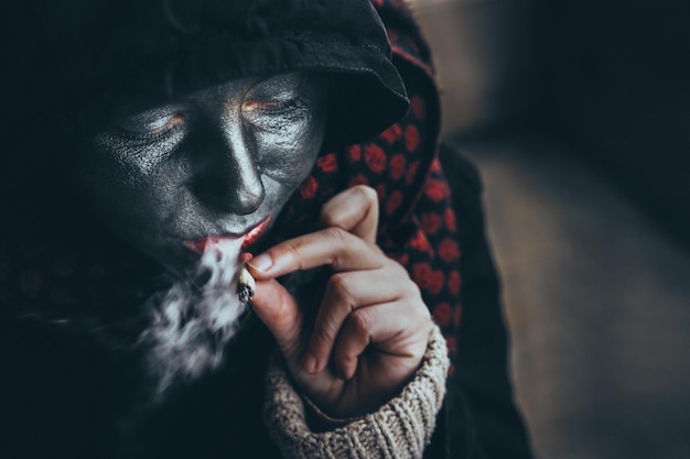 Primer plano de una mujer con pintura facial fumando un cigarrillo