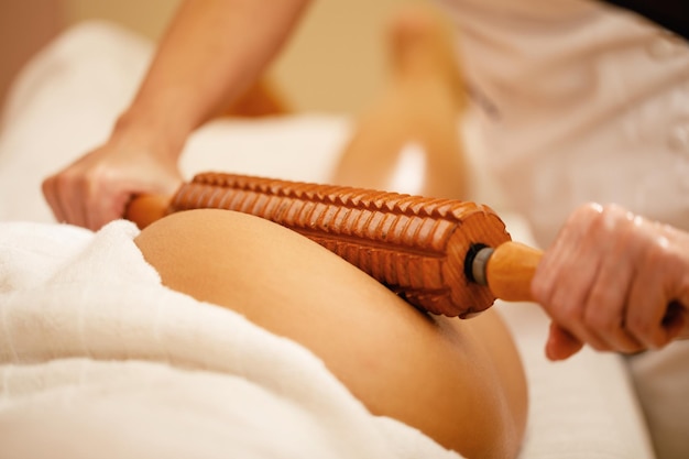 Foto primer plano de una mujer que recibe un masaje en las nalgas con un rodillo de madera durante la maderoterapia en el spa