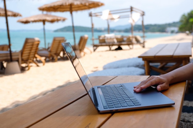 Primer plano de una mujer que trabaja y toca el panel táctil de la computadora portátil en la playa