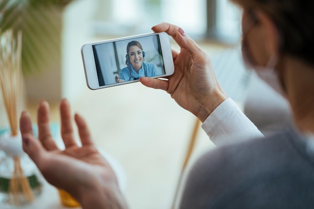 Primer plano de una mujer que usa un teléfono inteligente y tiene una videollamada con un trabajador de la salud durante una pandemia de virus