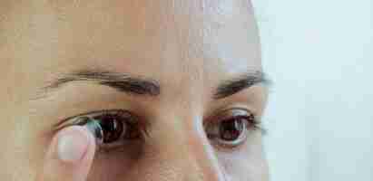 Foto primer plano de una mujer quitando lentes de contacto blandos de su ojo sobre un fondo blanco.
