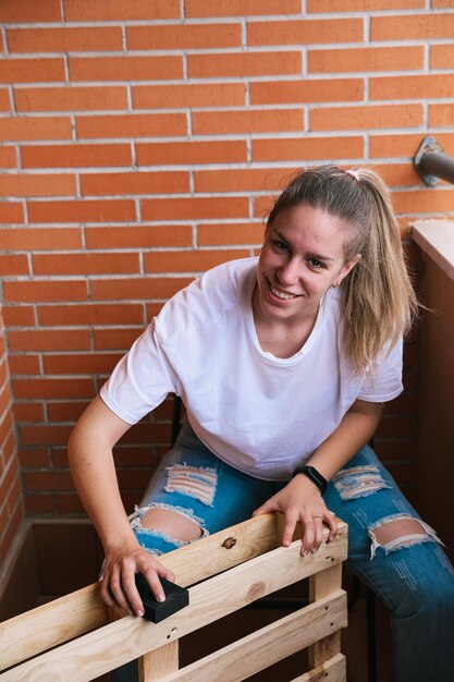 Foto el primer plano de una mujer rubia lijando con papel de lija a mano un palet en la terraza renovación del hogar