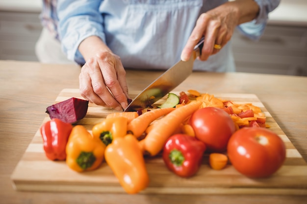 Primer plano de mujer senior para picar verduras en la cocina