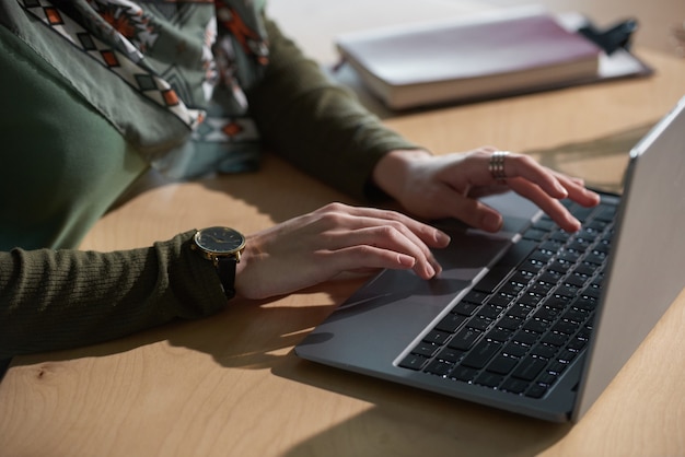 Primer plano de una mujer sentada en la mesa y escribiendo en la computadora portátil durante su trabajo en la oficina