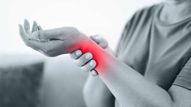 Primer plano de una mujer sentada en el sofá sostiene su muñeca, lesión en la mano con resaltado rojo, sintiendo dolor. Cuidado de la salud y concepto médico.