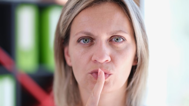 Primer plano de una mujer seria que muestra el signo shh con el dedo o para guardar silencio gesto mujer sosteniendo