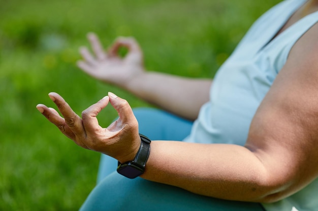 Primer plano de una mujer con sobrepeso irreconocible haciendo yoga al aire libre y meditando con enfoque en las manos c