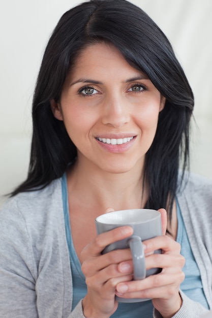 Primer plano de una mujer sonriendo mientras sostiene una taza