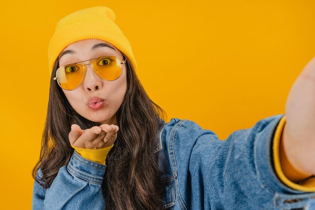 Primer plano de mujer sonriente haciendo foto selfie en smartphone aislado sobre fondo amarillo