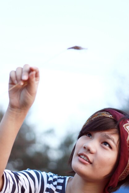 Foto primer plano de una mujer sonriente mirando una planta contra el cielo