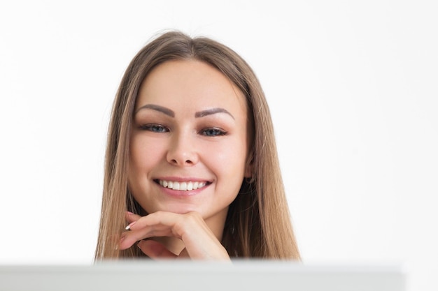 Primer plano de una mujer sonriente en una oficina. Ella está mirando la pantalla de su computadora portátil y sonriendo. Fondo blanco.