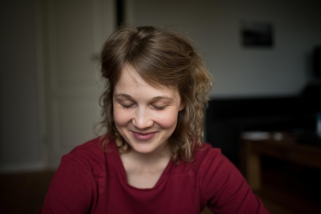 Primer plano de una mujer sonriente con los ojos cerrados sentada en casa