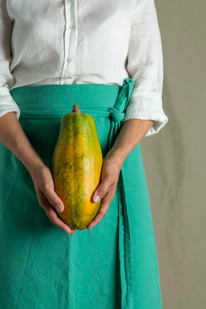 Primer plano de una mujer sosteniendo una fruta de papaya contra un fondo liso foto de archivo