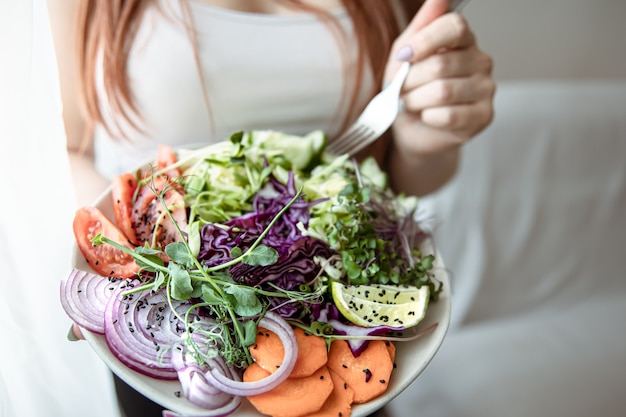 Primer plano de una mujer sosteniendo un plato grande de ensalada de verduras recién preparada en casa.