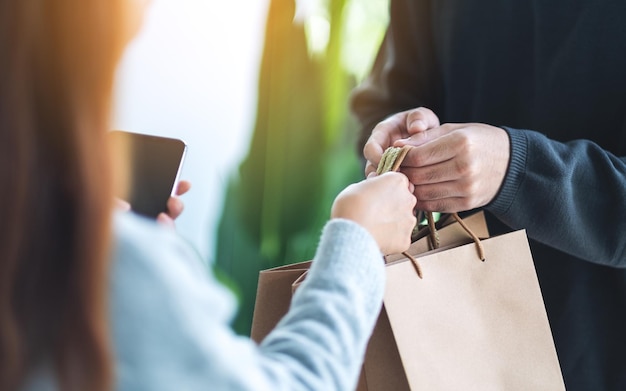 Primer plano de una mujer sosteniendo un teléfono móvil y recibiendo bolsas de compras del repartidor