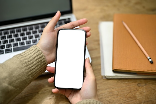 Primer plano de una mujer en suéter acogedor usando su teléfono inteligente en su escritorio