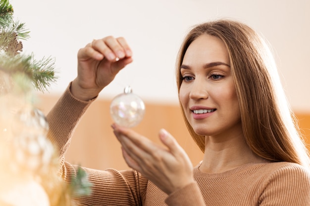 Primer plano de una mujer en suéter decorar el árbol de navidad