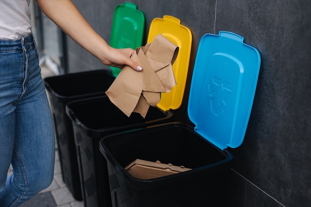 Primer plano de una mujer tirando un trozo de cartón en la papelera de reciclaje de diferentes colores de papeleras de reciclaje