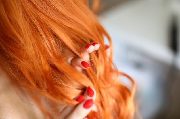 Primer plano de mujer tocando el pelo rojo. Mujer con hermosa manicura fresca. Bonitos rizos en la cabeza. Buen volumen y ondas después del rizador. Lindo peinado. Concepto de belleza