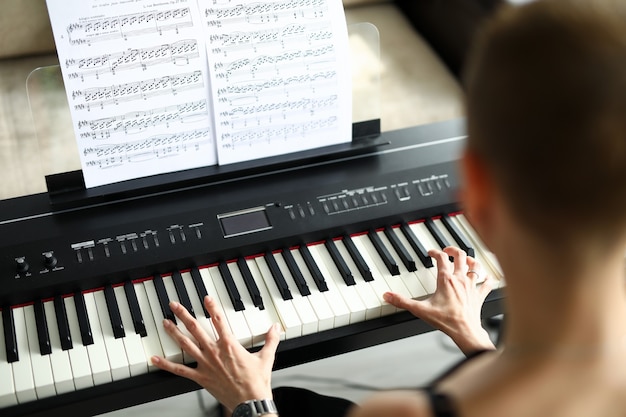 Primer plano de una mujer tocando un piano eléctrico. llave en blanco y negro. partitura con canción. ejercicio de mujer joven en casa. tiempo libre y concepto de hobby