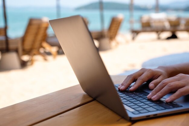 Primer plano de una mujer trabajando y escribiendo en una computadora portátil en la playa