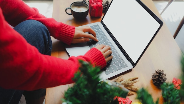 Primer plano de una mujer usando una computadora portátil mientras toma café durante la Navidad