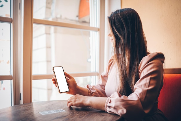 Primer plano de una mujer usando un teléfono celular enviando masajes en la cafetería