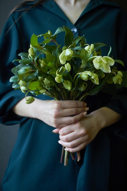 Primer plano de una mujer en un vestido verde con un ramo de flores de eléboro en flor fresca, enfoque selectivo
