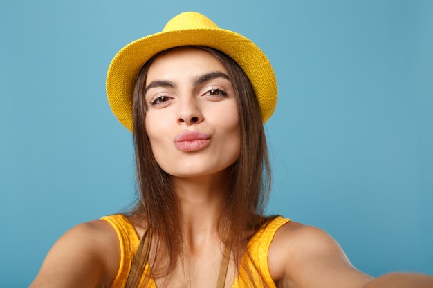 Primer plano mujer viajera en ropa casual de verano amarillo y sombrero haciendo selfie en teléfono móvil posando en azul