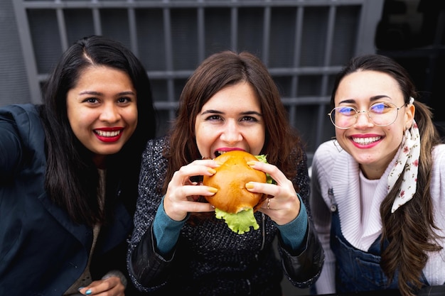 Primer plano mujeres jóvenes sentados en el restaurante y tomando un retrato selfie mientras comen una hamburguesa.