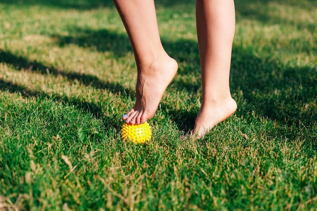 Primer plano de las mujeres pies descalzos de pie sobre una bola de masaje con púas para relajarse o arreglar los pies planos sobre la hierba verde en el parque de verano